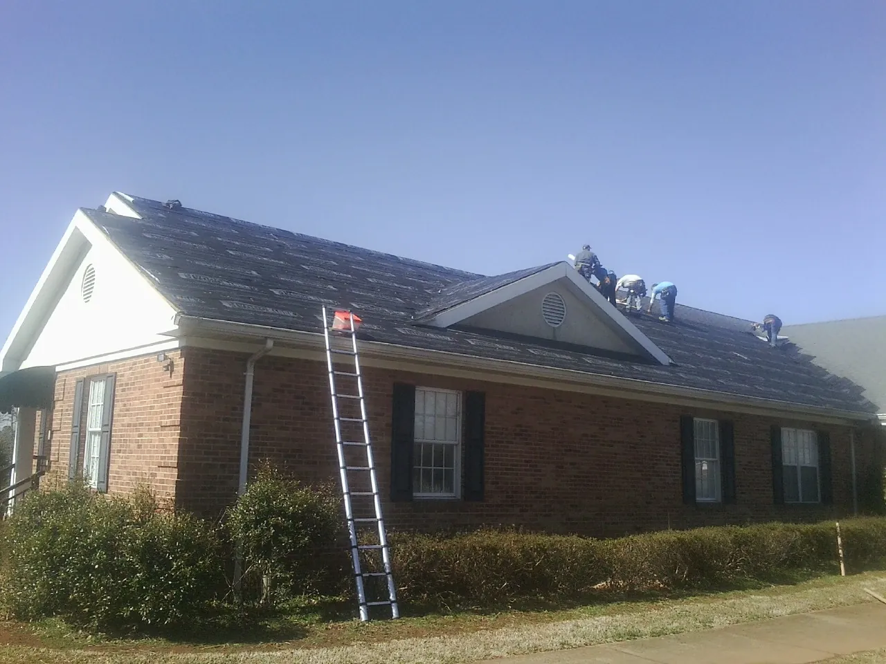 Crew tearing shingles off a brick ranch roof with a ladder set — Metal Roof Repair work by our crew in Mangum
