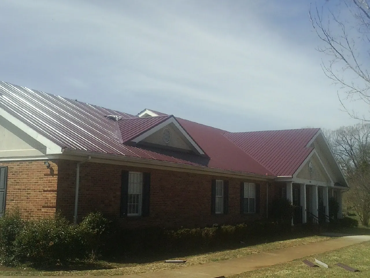 Red metal roof with gabled entries on a long brick building, from a Hail Damage Roof Repair job in Mangum