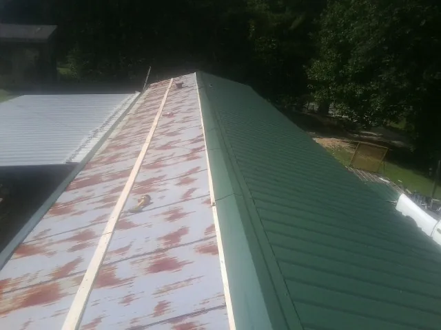 Old rusted panels beside newly installed green metal roofing — Wind Damage Roof Repair by Roofing Brothers in Mangum