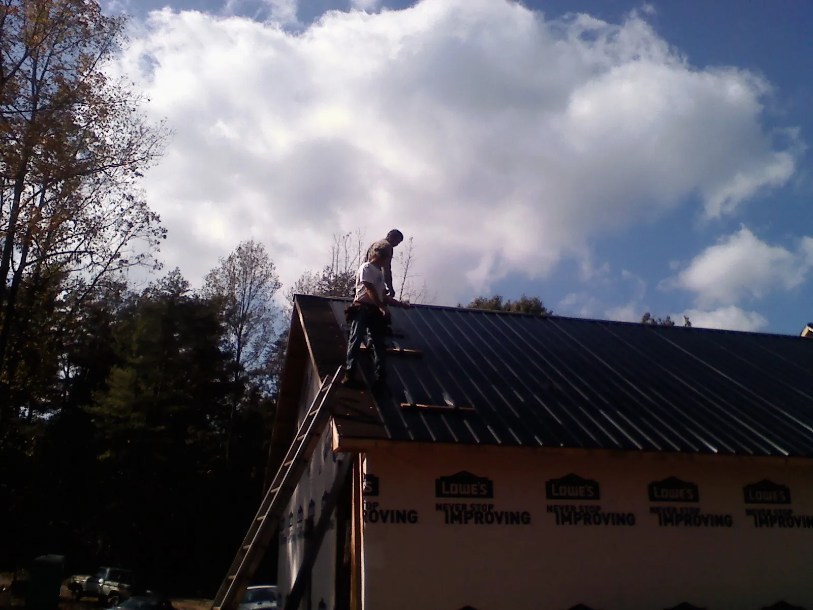 Roofer fastening dark metal panels high against a cloudy sky, from a Roof Inspection job in Mangum