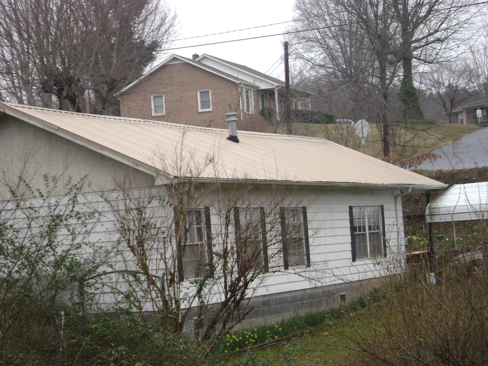 Tan metal roof on a white sided house set into a hillside — Commercial Roofing by Roofing Brothers in Mangum
