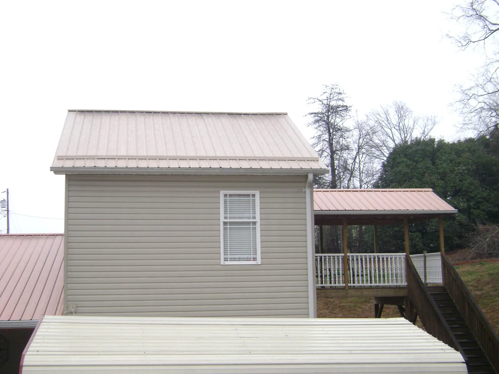 Tan metal roofs on a two story addition and attached porch, from a Roof Replacement job in Mangum